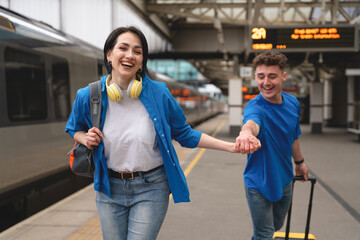 Young couple joyfully walking hand in hand at train station, ready for an adventure on a sunny day