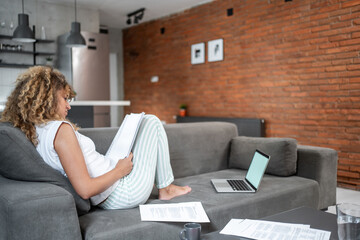Obraz premium Young woman reading documents while relaxing on sofa at home
