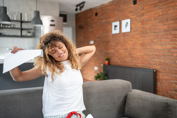 Woman waking up and stretching on sofa holding paper at home