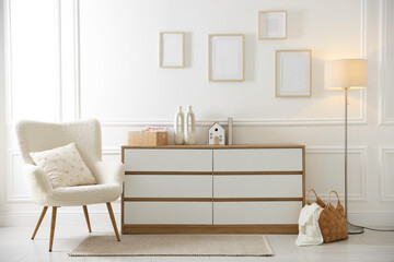 Blank frames on wall, armchair and chest of drawers indoors