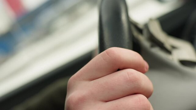 close up of fair skin hand gently tapping steering wheel with finger while holding it during daytime inside car with blurred abstract background through window