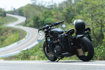 Obraz premium A black motorcycle parked on the roadside with a winding road and lush greenery in the background.