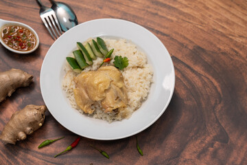 Steamed rice topped with chicken in a white plate on a wooden table