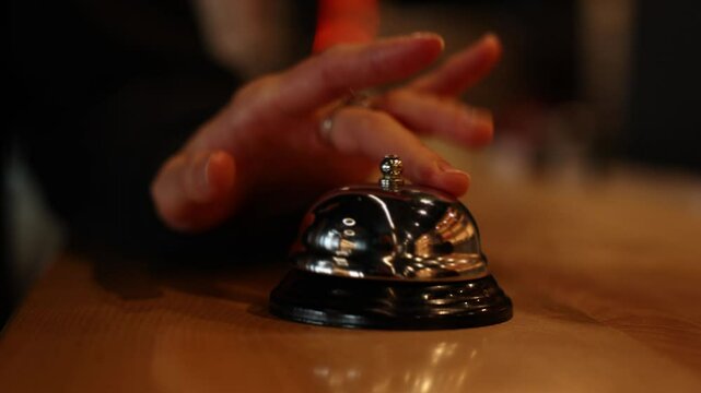 Close up hand of unrecognisable woman impatiently pressing the bell at hotel reception desk. Ring bell for customer service, hospitality and help. Check in, welcome and help with service alert.