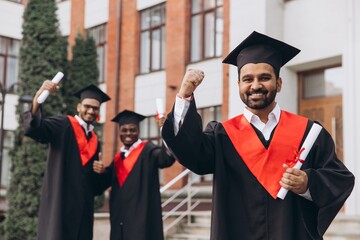 Three Graduating Students Celebrating Their Success with Diplomas Outdoors at University Campus
