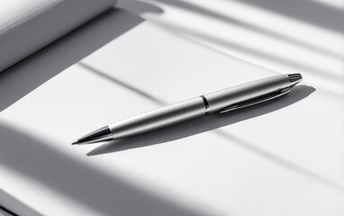 Sleek silver pen resting on a blank notebook with soft shadows from nearby window blinds