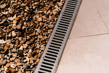An impeccably clean drainage grate situated next to beautifully arranged decorative gravel and...