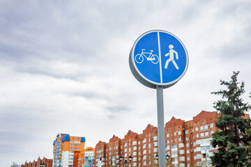 Road separation sign bicycle lane and pedestrian path. Cityscape with houses and overcast sky. 