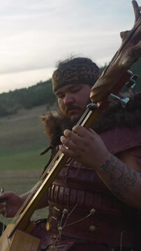 Large man in shaman costume plays ikili sitting in mountain valley at sunrise light. Siberian folks music at festival. Protecting old traditions
