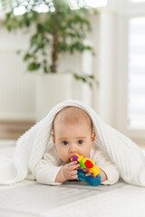 Baby care concept. Baby exploring colorful toy while playing on soft blanket indoors
