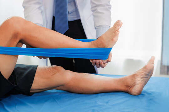 An elderly patient undergoes leg physiotherapy on a treatment bed while being carefully assisted and advised by a healthcare specialist.