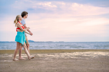 Romantic couple walking hand in hand on beach at sunset, casting long shadows on sand, with ocean waves gently rolling in. Suitable for travel and emotional connection concepts.