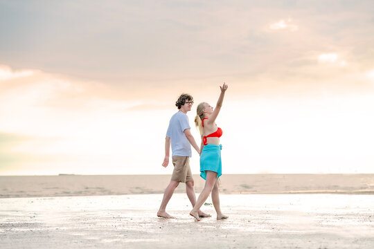 Loving partners strolling on beach, hand in hand, with clear blue sky and calm sea setting a tranquil backdrop. Perfect for romantic and vacation imagery. - Powered by Adobe