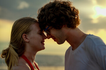 Fototapeta premium A white couple touches foreheads lovingly at the beach during sunset. The golden light and ocean backdrop highlight their emotional connection and romantic intimacy.