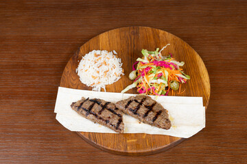 Kefte with mozzarella cheese, Turkish rice with meat with adjika, mixed salad and local minced meat kebab on the restaurant table on a wooden stand
