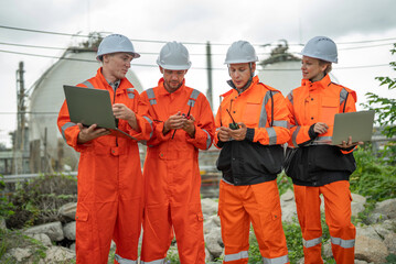 caucasian white engineers in safety uniforms and helmets using laptop and radio for site communication. Concept of teamwork, inspection, and operations at an industrial facility.Construction of Oil, 