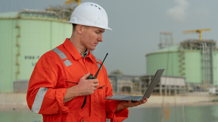 caucasian white engineers in safety uniforms and helmets using laptop and radio for site communication. Concept of teamwork, inspection, and operations at an industrial facility.Construction of Oil, 
