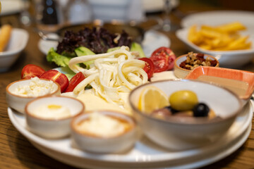 Close up view of a mixed breakfast plate with various foods, including cheese, jams, butter, honey, walnuts, tomatoes, and olives, on a restaurant table.