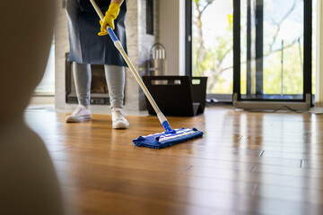 Person cleaning wooden floor with mop in bright living room during daytime