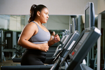 Fat woman exercising on a treadmill in a gym, wearing a grey sports bra and black leggings.