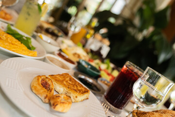 Close up view of a slice of pastry with feta cheese filling and small Turkish pizza snacks with minced meat and cheese on a white plate on a breakfast table.