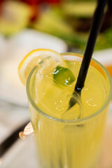 A glass of lemonade with ice, a lemon slice, fresh mint, and a straw is served on a restaurant table.