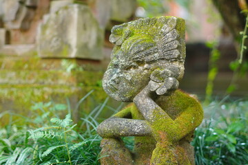 A statue carved from stone posing like a person supporting his chin while sitting with a Balinese...