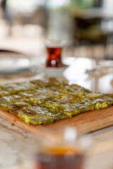 Traditional Turkish dessert Katmer with clotted cream and dough served with tea on a restaurant table. Prepared with thin dough, green ground pistachio and sherbet. Dessert of Gaziantep region.