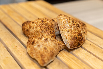 Close up view of freshly baked, hot, small loaves of bread on a wooden table in a bakery kitchen.