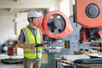 An Asian male engineer is working in front of a punch press.