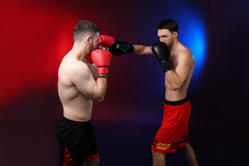 Men with boxing gloves fighting on dark background in neon lights