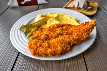 Pork schnitzel with mashed potato and pickled cucumber.