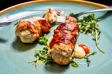Fried pork roll stuffed with cheese and bacon, rucola leaf on blue plate with cutlery.