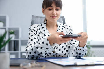 Woman taking photo of document using scanning app on smartphone at desk in office