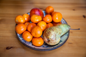 Citrus fruit bowl with pear on wooden table.