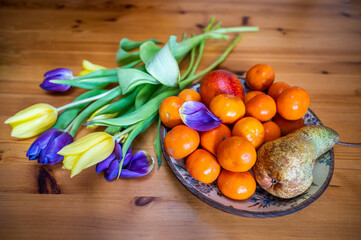 Tulip bouquet and citrus fruit bowl with pear on wooden table.