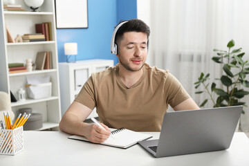 Man taking notes during online lesson at desk indoors. Self-study