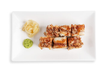 Top view of sushi rolls or unagi maki made from eel fish, rice, seaweed and cream cheese decorated with bonito flakes served on rectangular plate with ginger and wasabi isolated on white background