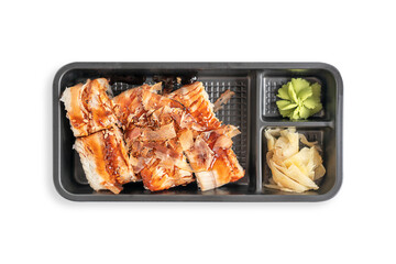 Top view of black delivery take away container lunch box with set of unagi maki or sushi rolls with eel fish decorated with bonito flakes served with wasabi and ginger isolated on white background