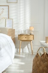 Bedside table with lamp, jug of water and glass near bed in room. Interior design