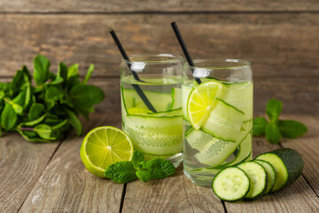 Cucumber water with lemon, lime and mint on a wooden table. Water infused with sliced ​​cucumber in a drinking glass. Tonic refreshing drink. Cucumber lemonade.Summer natural cooling drink.Copy space