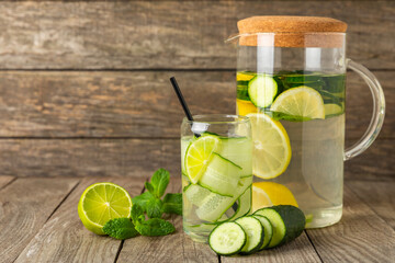 Cucumber water with lemon, lime and mint on a wooden table. Water infused with sliced ​​cucumber in a drinking glass. Tonic refreshing drink. Cucumber lemonade.Summer natural cooling drink.Copy space