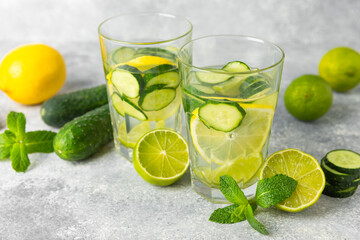 Cucumber water with lemon, lime and mint on a wooden table. Water infused with sliced ​​cucumber in a drinking glass. Tonic refreshing drink. Cucumber lemonade.Summer natural cooling drink.Copy space