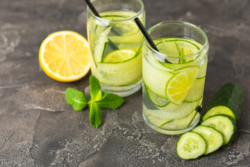 Cucumber water with lemon, lime and mint on a wooden table. Water infused with sliced ​​cucumber in a drinking glass. Tonic refreshing drink. Cucumber lemonade.Summer natural cooling drink.Copy space