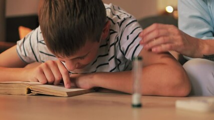 Supportive mother helping son develop reading skills, providing gentle encouragement while tracking learning progress with hourglass timer in cozy home environment
