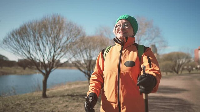 Portrait of happy old lady with poles for nordic walking in park in motion. Active lifestyle and sport activity for stay healthy and positive in old age, good feeling and mood, aged woman keeping fit