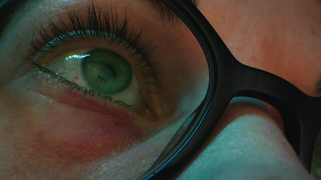 Close up of tired woman working at night on laptop, girl in eye glasses with reflections overworking busy, using computer in dark office