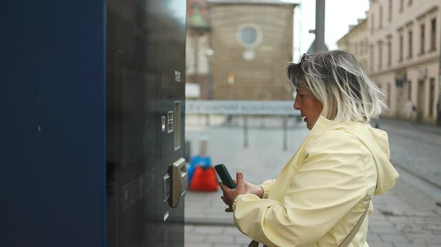 Elderly woman purchasing a tram ticket at a vending machine on a city street in Krakow, Poland. A modern urban moment highlighting independence, public transportation, and everyday travel routines.