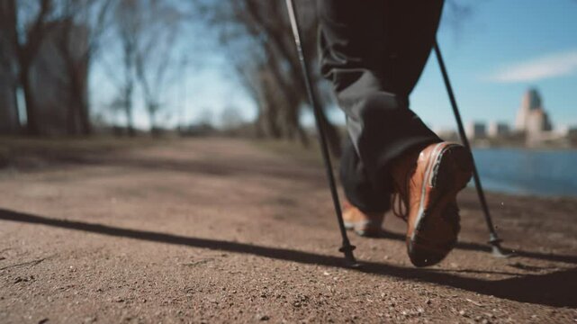 Nordic walking in park, closeup of feet of aged person, grandmother training. Slow motion shot with mature woman legs stepping on ground of recreation area in city, do sport and live healthy life