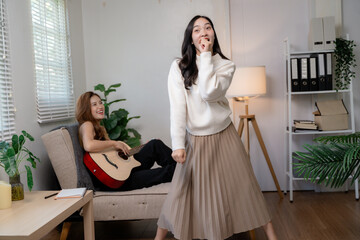 Asian women are enjoying their free time playing the guitar and singing in the living room
